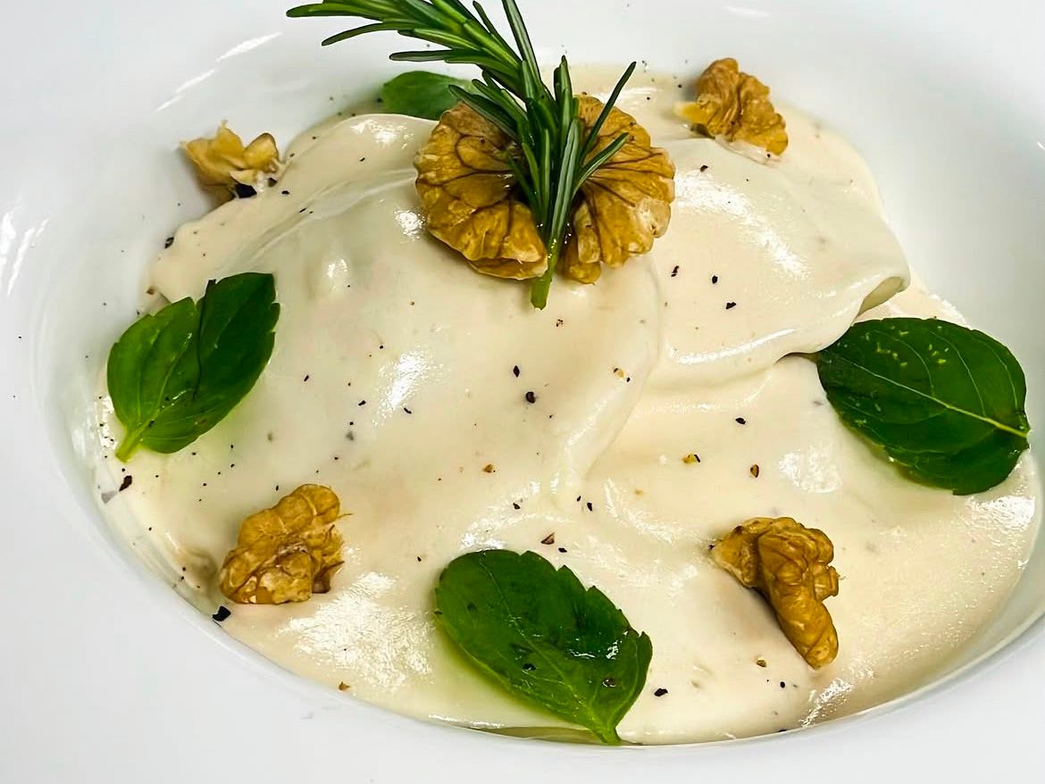 Ravioli sem glúten de nozes com pêras caramelizadas no mel, coberto com molho bechamel vegano, nozes e manjericão.