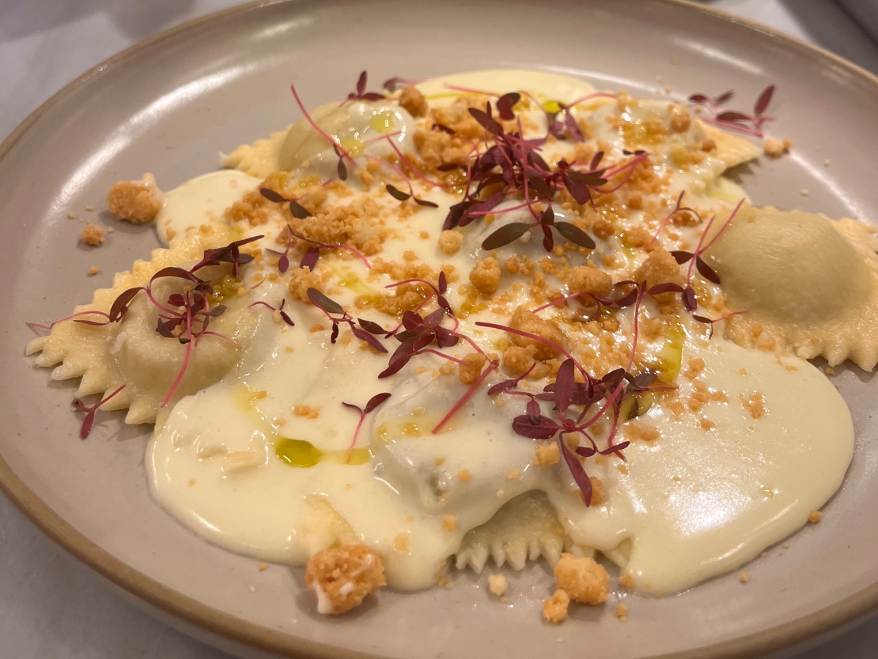 Ravioli de costela com fonduta e crumble de parmesão, finalizado com azeite de manjericão e folhas de amaranto